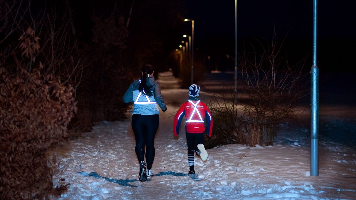 Två personer motionerar i mörkret med tydliga reflexer